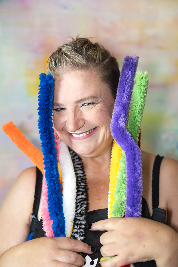 Create your Space with Shara - Shara, art therapist with large coloured pipe cleaners, smiling at the camera