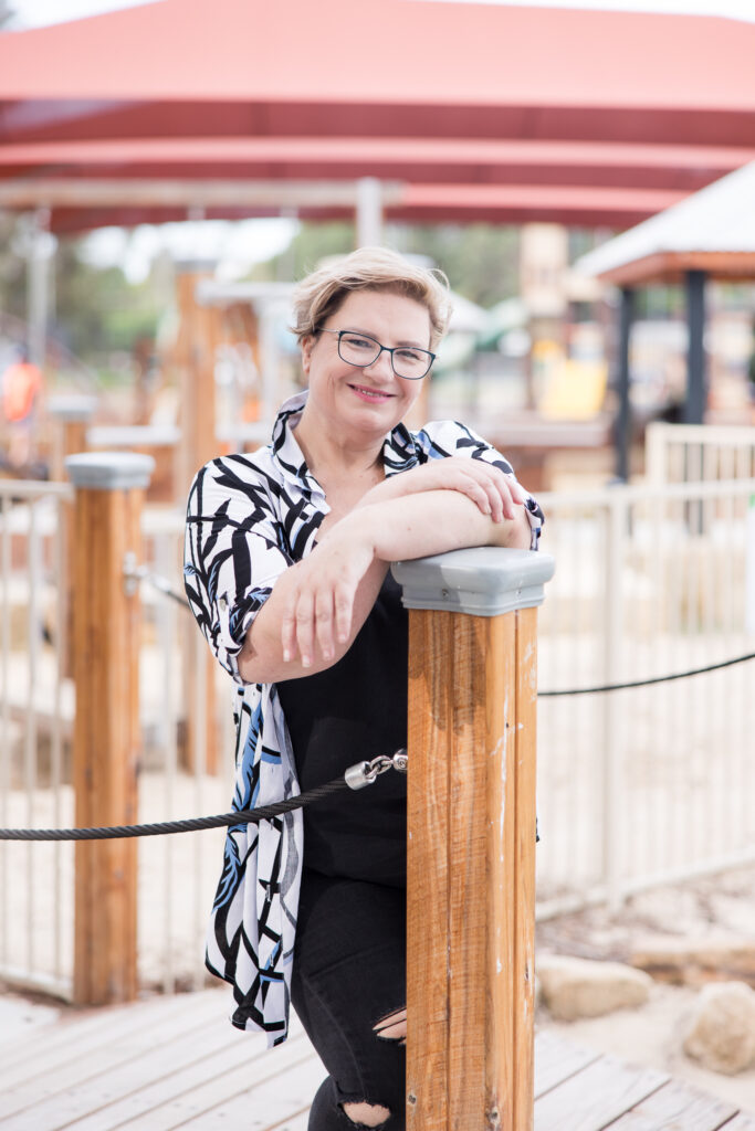 Create your Space with Shara - Shara  wearing a patterned shirt and glasses, leaning against a post in a playground.