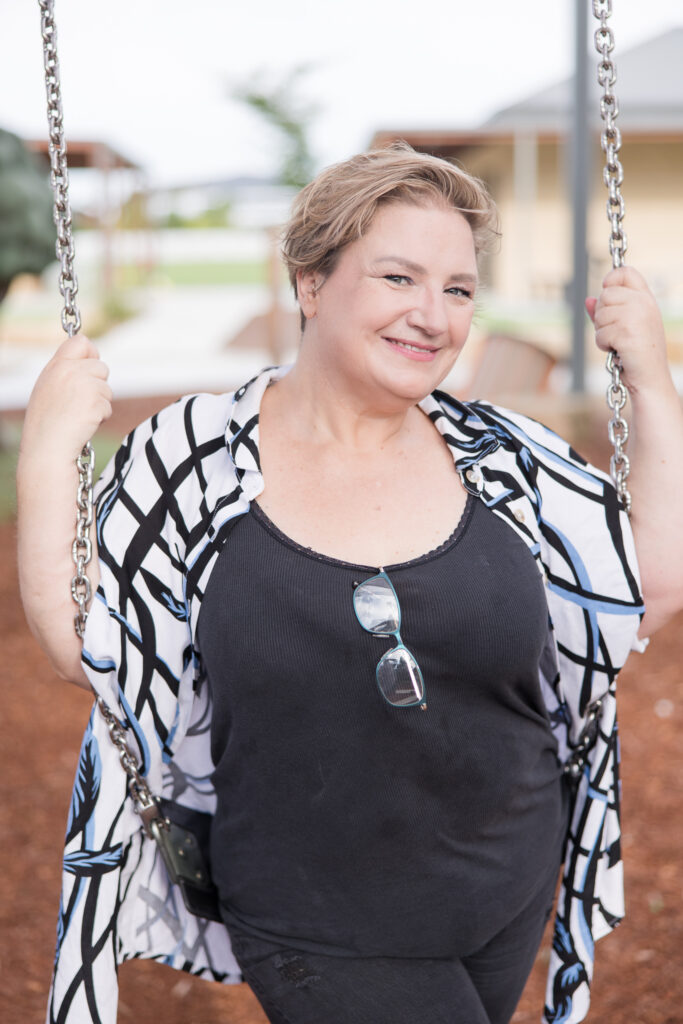 Create your Space with Shara - Shara wearing a patterned shirt sitting on a swing, smiling at the camera.