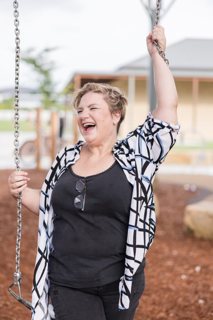 Shara wearing a patterned top,sitting on a swing and laughing.