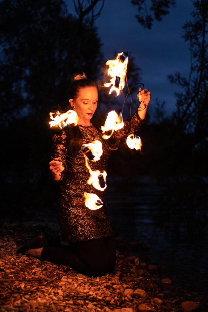 Photograph of a woman kneeling in the dark and fire twirling