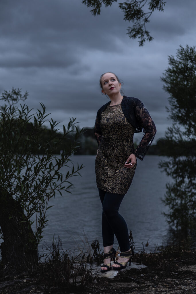 Woman standing by lake with cloudy sky