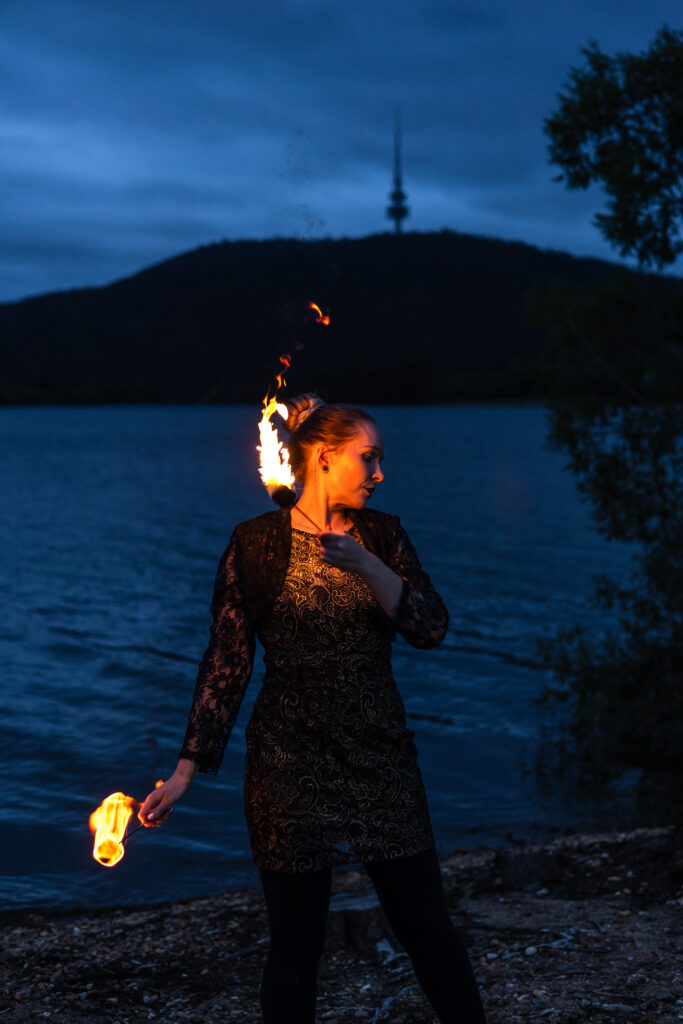 Photograph of a woman standing by a lake fire twirling