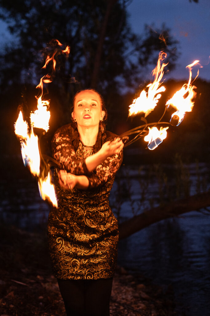 Photograph of a woman standing in dark with arms crossed and face illuminated by fire twirling