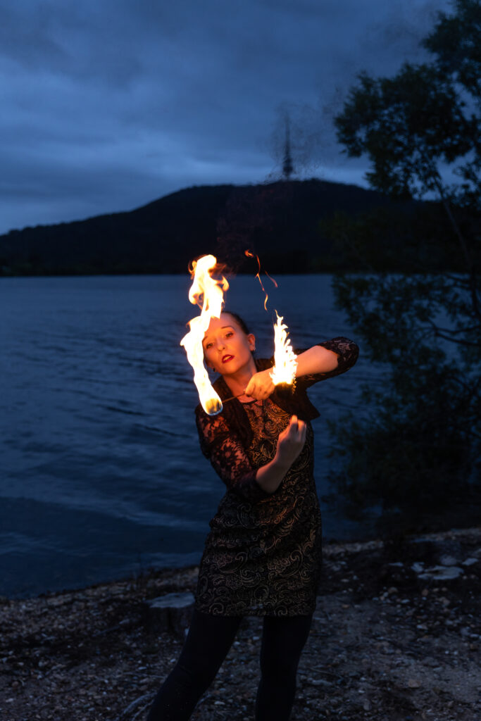 Photograph of a woman standing next to a lake fire twirling