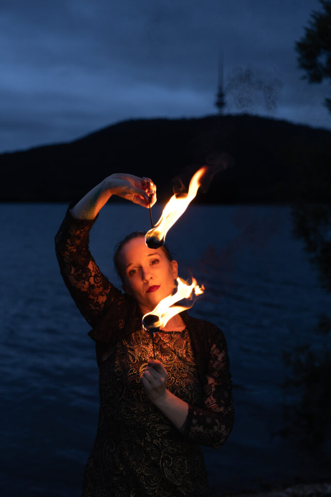 Photo of a woman standing by a lake with face illuminated by fire twirling