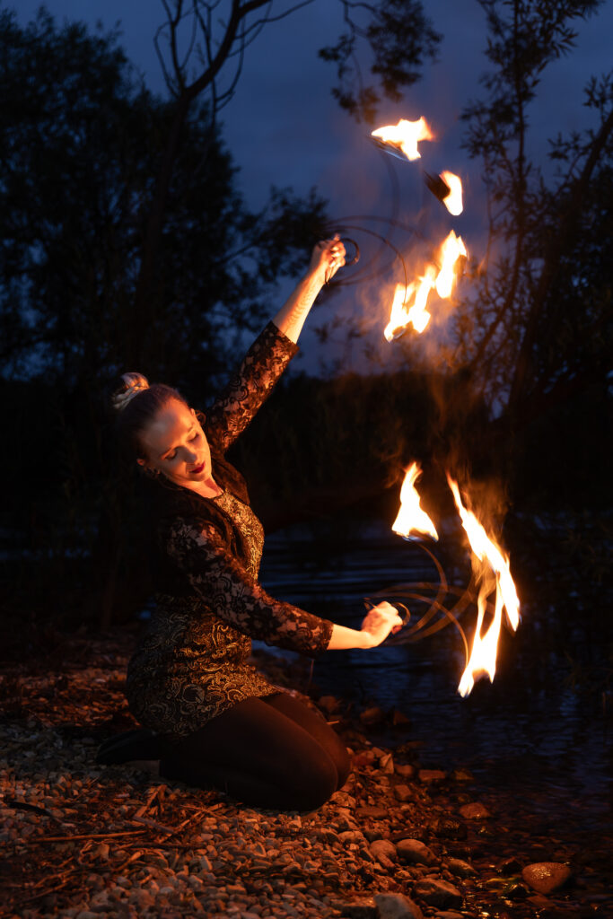 Photograph of a woman kneeling near water and fire twirling