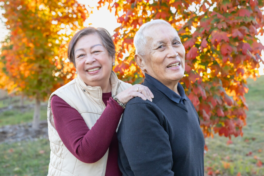 Older man and woman in front of autumn trees, smiling