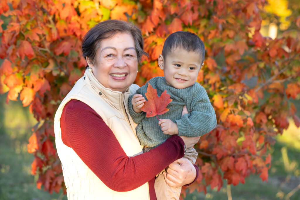 Grandmother holding a toddler who has an autumn leaf in his hand at National Arboretum, Canberra