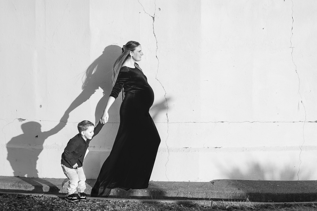 Mother-to-be holding her son's hand with shadows against the wall of the Mt Stromlo Observatory during a maternity photo session.